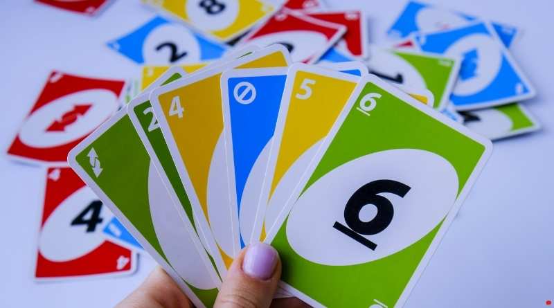 En hand håller upp ett UNO-kort framför en utspridd kortlek i rött, gult, blått och grönt – symbolen för det populära kortspelet UNO.